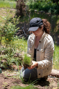 Skylar Lipman, wearing a black hat and khaki shirt, kneeling a garden with plants in the background